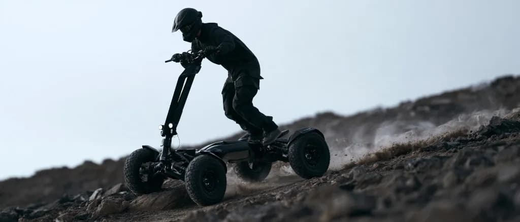 A rider on the all terrain electric scooter riding down a steep rocky slope, throwing up dust behind the four knobbly tyres.